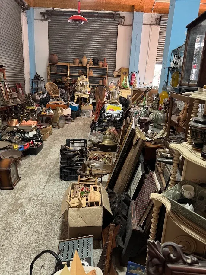Pasillo de la nave de la tienda con cerámica, butaca de mimbre, relojes y muebles antiguos