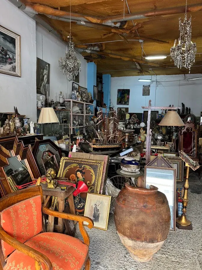 Lámparas de araña, tinaja de barro, butaca tapizada y cuadros en la tienda de antigüedades de Zaragoza